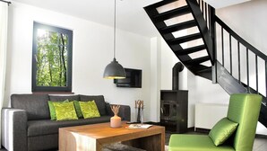 Una sala de estar con un sofá, una mesita de centro y un sillón verde. Se ve una escalera negra al fondo.