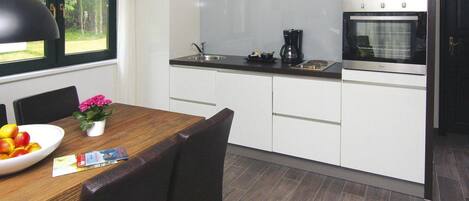A modern kitchen with white cabinets, a wooden dining table, and a black pendant light.
