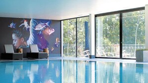 Una piscina interior con un mural, sillones de descanso y grandes ventanales que ofrecen vistas al exterior.