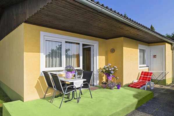 A yellow building with a green lawn, a table with chairs, a red and white checkered lounge chair, and a white door. - Bungalow on Lake Klopein With a Terrace (Sankt Kanzian am Klopeiner See)