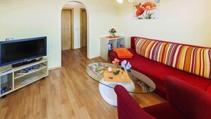 A living room with a flat-screen TV, a red sofa, a glass coffee table, and a bookshelf. - Bungalow on Lake Klopein With a Terrace (Sankt Kanzian am Klopeiner See)