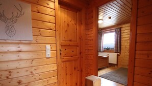 A wooden cabin interior with a wooden door, a wall-mounted light switch, and a window with curtains. - Doppelhaushalfte in Hasselfelde (Oberharz am Brocken)