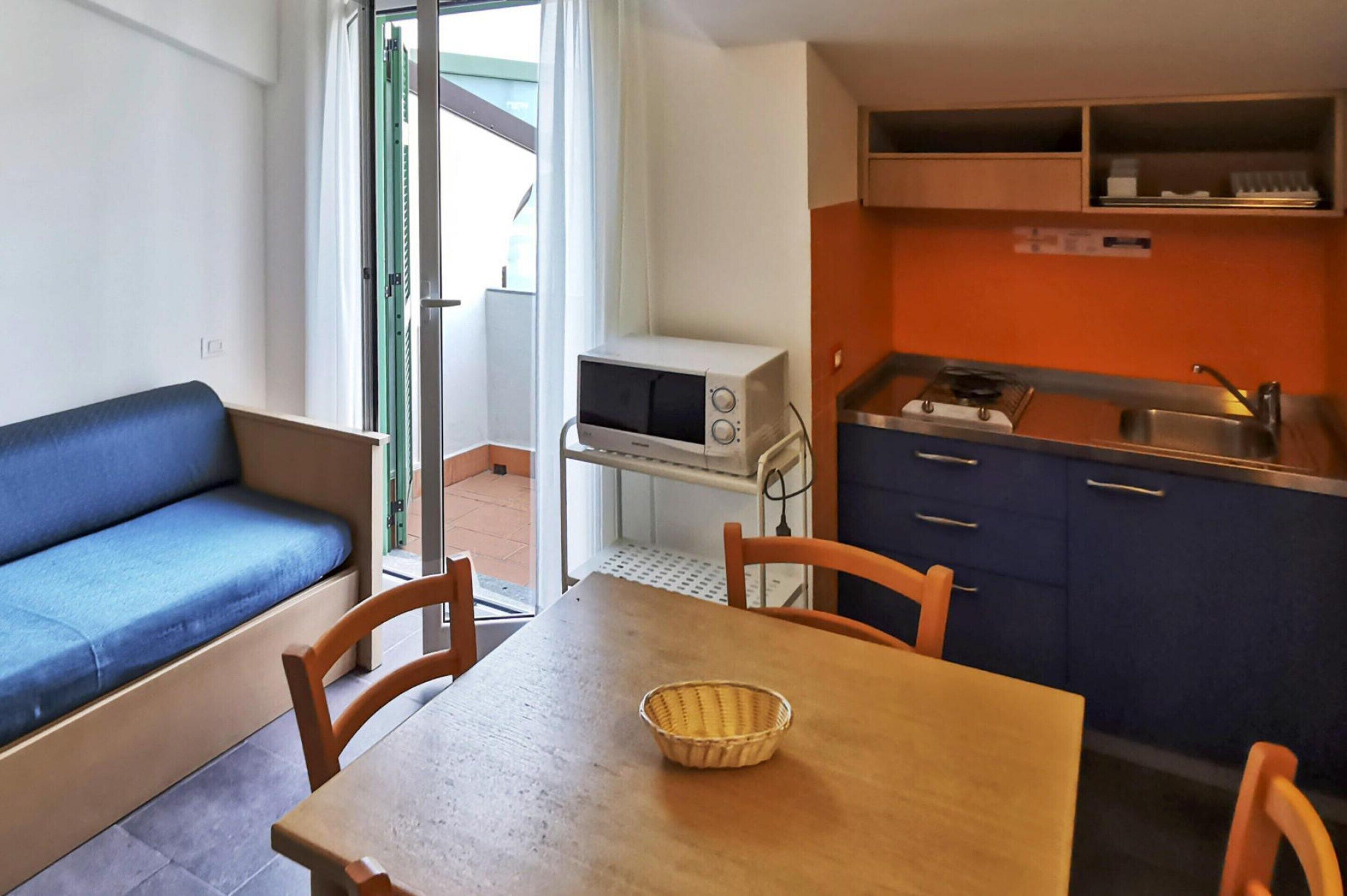 A compact living space with a kitchenette, a dining table with chairs, a blue sofa, and a microwave.
