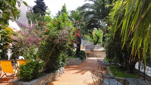A patio area with stone planters, metal chairs, and a pathway leading to a building entrance. - Apartment in Pietra Ligure (Pietra Ligure)