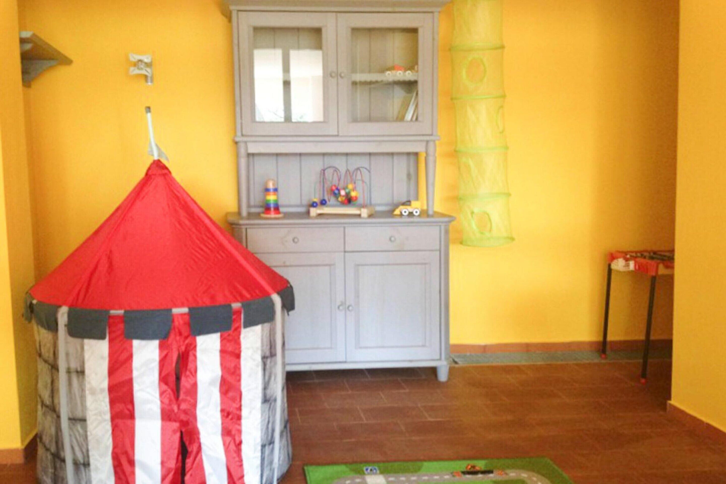 A room with a red and white striped tent, a grey cabinet with glass doors, and a yellow wall.