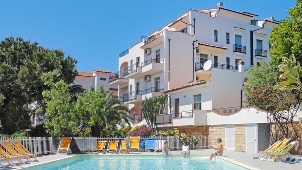 A swimming pool area with lounge chairs and a building with balconies. - Apartment in Pietra Ligure (Pietra Ligure)