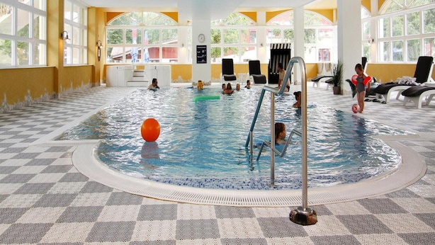 An indoor swimming pool with clear water, a checkered floor, and a poolside area with lounge chairs and a lifeguard stand. - Ferienpark Markgrafenheide (Rostock)