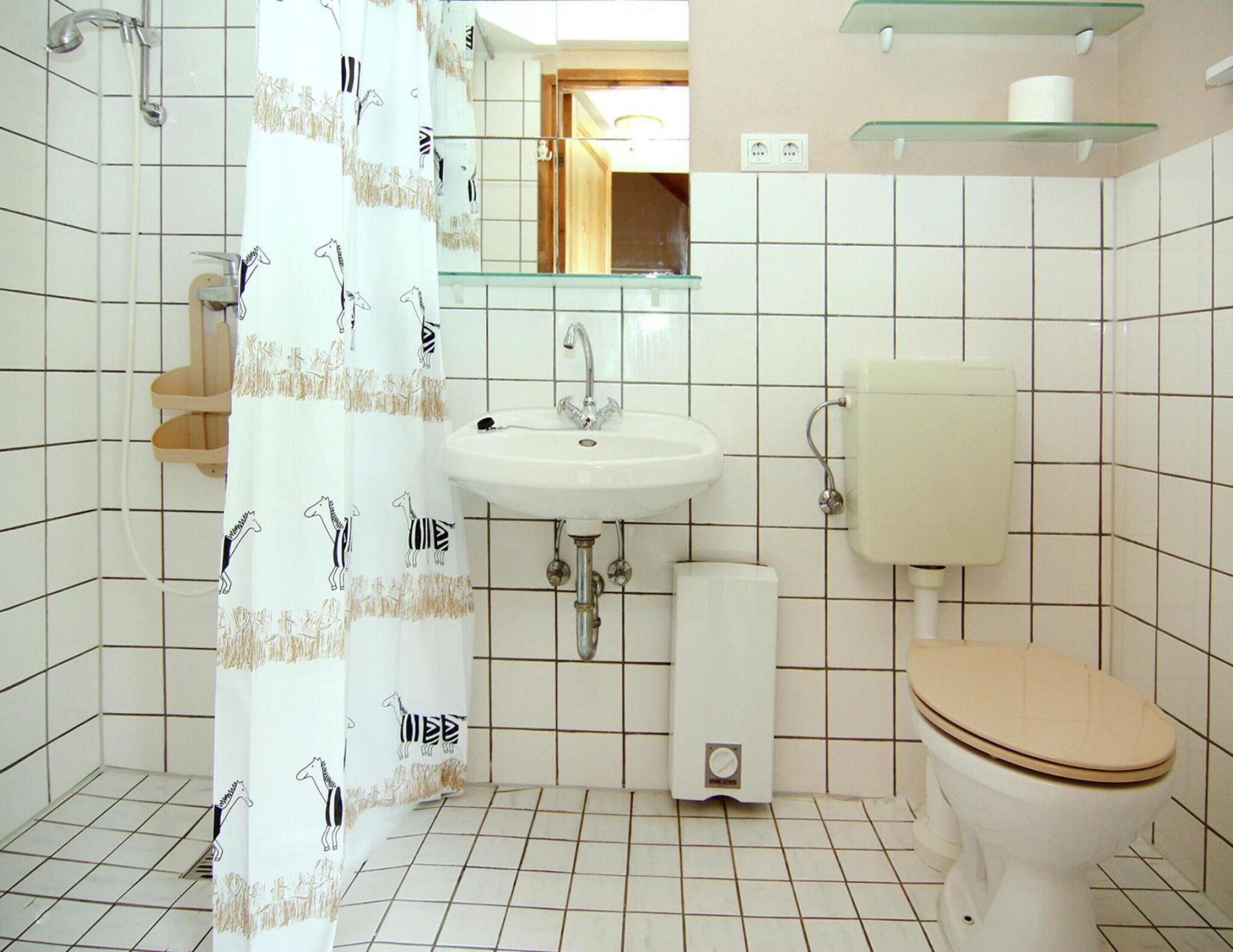 Ein Badezimmer mit weißem Waschbecken, Toilette und Dusche. Über dem Waschbecken befindet sich ein Spiegel und eine Handtuch an der Wand.