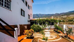 A courtyard with a white building, a stone fountain, and a view of distant hills. - Tenerife Coastal Vacation Home for 3 (Candelaria)