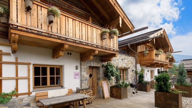 A wooden chalet with a balcony, stone walls, and outdoor seating.