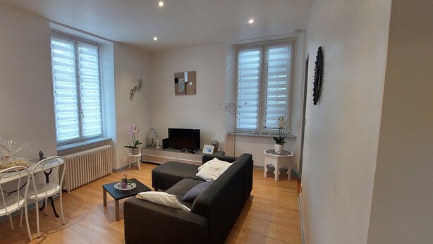 En stue med en sort sofa, et hvidt spisebord med stole, et fjernsyn og en radiator.