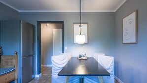 A dining area with a table, chairs, a hanging light fixture, and a framed artwork on the wall.