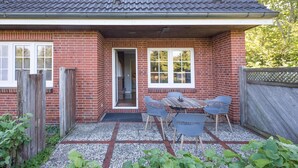 A brick house with a tiled roof, a covered patio with a table and chairs, and a wooden fence.