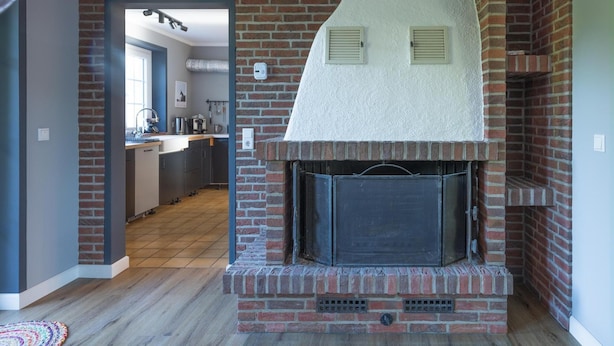 A modern kitchen with a brick fireplace, wooden flooring, and a view into the dining area.