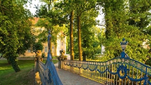 Un puente con barandillas azules ornamentadas y un sendero de piedra que conduce a un edificio de arquitectura clásica.