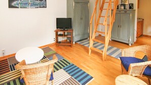 Una habitación con una escalera de madera, un televisor sobre un mueble de madera, sillas de mimbre y una alfombra a rayas.