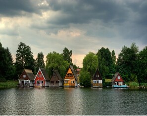 A row of traditional houses by a lake with a cloudy sky. - Ferienhaus im Mueritz-nationalpark (Mirow)