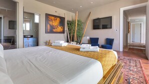 Una camera d'albergo con un letto grande, una televisione fissata al muro, uno specchio e una pianta.