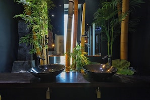 A dimly lit room with a dark wooden counter, two large metal bowls, and tall bamboo plants. - 4179 Villa Sueño By Perle di Puglia (Palmariggi)