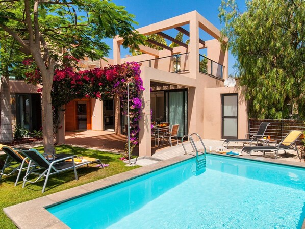 A modern poolside area with a clear blue pool, lounge chairs, and a pergola with flowering plants. - Bungalow With Communal Pool in Playa del Ingles (San Bartolomé de Tirajana)