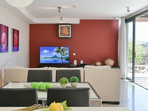 A modern living room with a large flat-screen TV, a sofa, a dining table with chairs, and a view of the outdoors through a sliding glass door. - Bungalow With Communal Pool in Playa del Ingles (San Bartolomé de Tirajana)