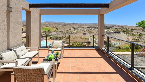 A balcony with a pool, outdoor furniture, and a view of a hilly landscape.