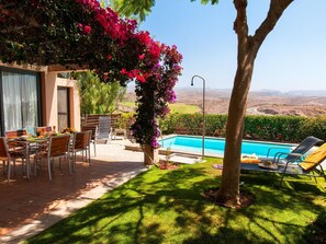 A poolside area with a dining table and chairs, a lounge chair, and a view of a mountainous landscape. - Bungalow With Communal Pool in Playa del Ingles (San Bartolomé de Tirajana)