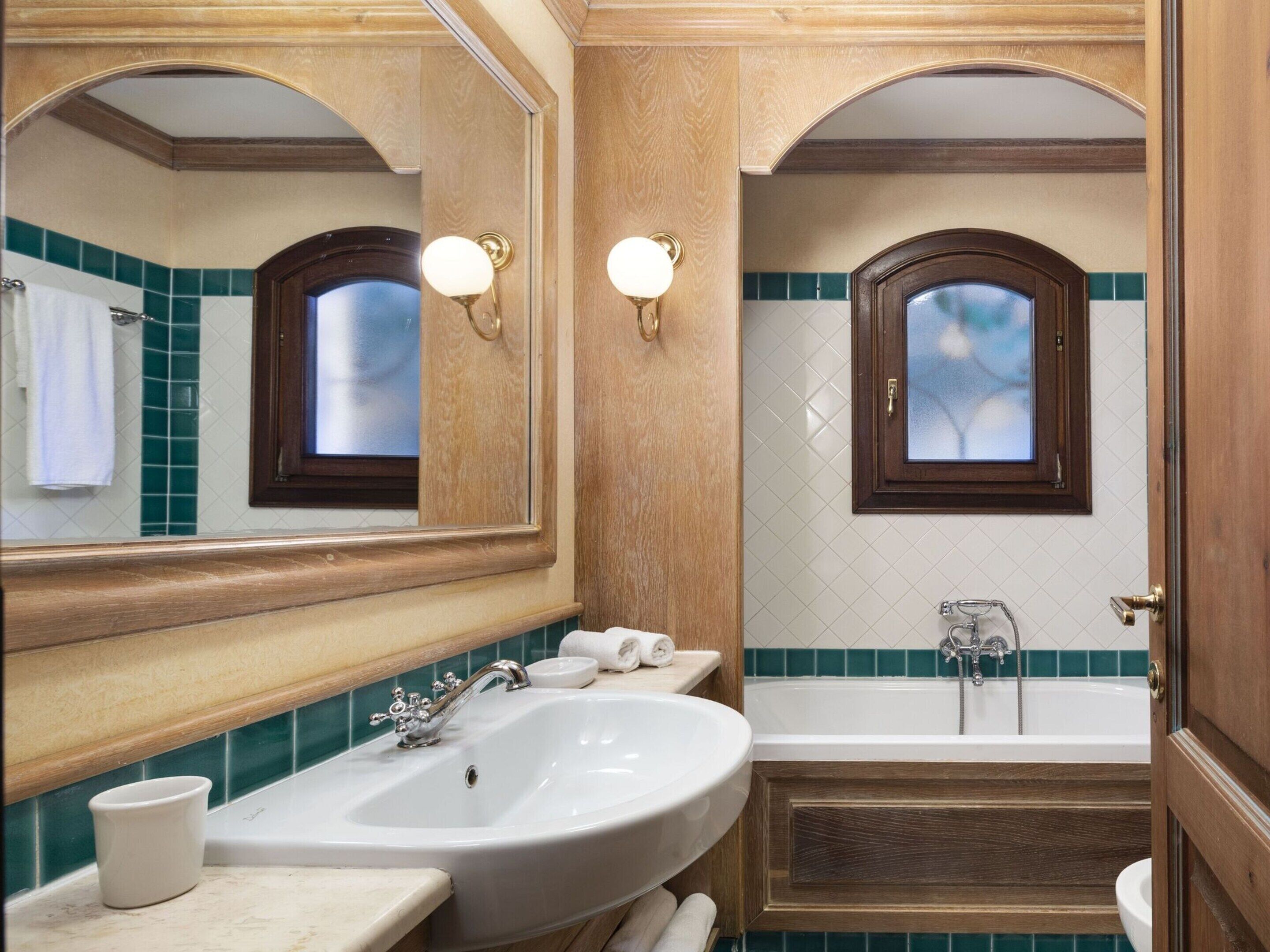 A bathroom with a large sink, a bathtub, and a mirror with two wall sconces.