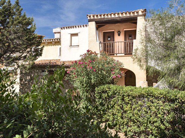 A two-story building with a balcony, stone walls, and a garden with pink flowers. - Holiday Residence Il Giardino Degli Oleandri in Porto Cervo (Arzachena)