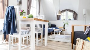 En moderne stue med spiseplads, med hvide møbler, et træbord og et stort vindue med gardiner.