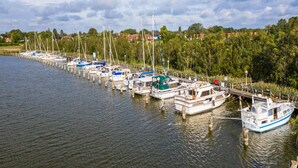 Ein Yachthafen mit mehreren Booten, die an einer Holzsteganlage vertäut sind, umgeben von Bäumen und Häusern im Hintergrund.