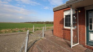 A brick building with a green door, a window, and a chain-link fence in front. - Holiday Bungalow in Dornumersiel (Dornum)