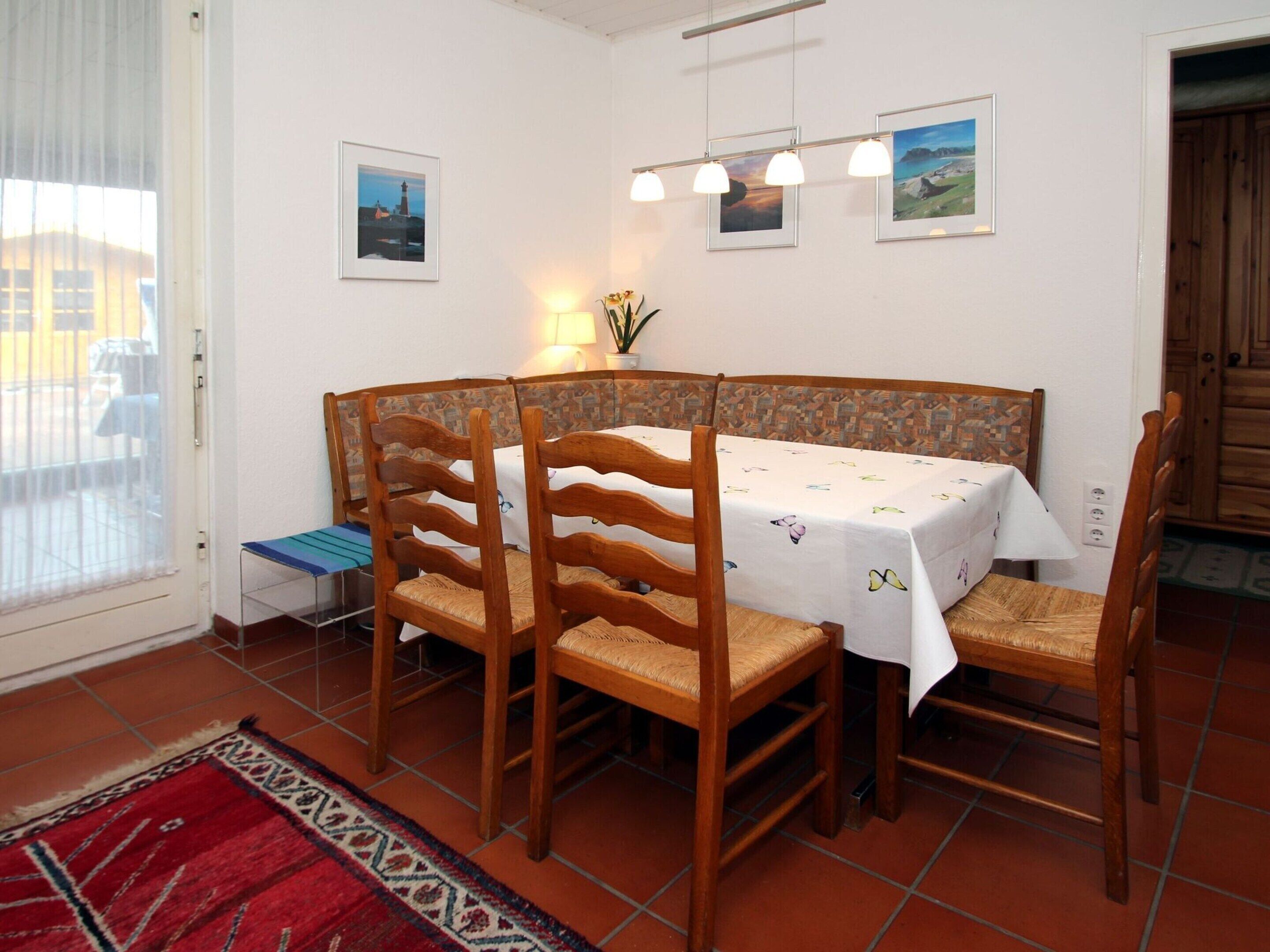 Un coin repas avec une table ronde, quatre chaises en bois, un tapis rouge à motifs et un mur orné de tableaux encadrés.