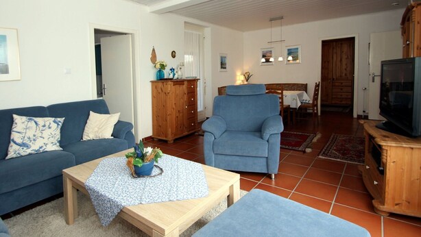 Un salon avec un canapé bleu, une table basse en bois, un fauteuil bleu et un téléviseur posé sur un meuble en bois.