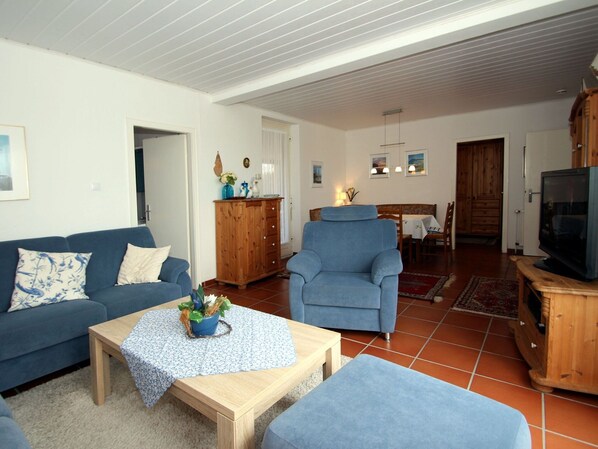 A living room with a blue sofa, a wooden coffee table, a blue armchair, and a television on a wooden cabinet. - Holiday Bungalow in Dornumersiel (Dornum)