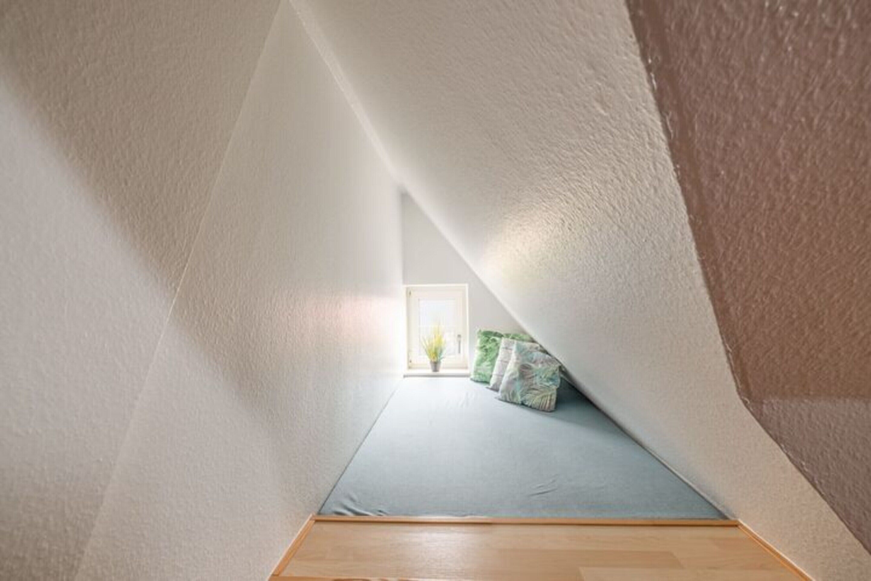 A narrow, sloped room with a low ceiling and a small window at the far end.
