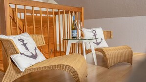 Ein Zimmer mit Korbmöbeln, einem Glastisch und einer Weinflasche.