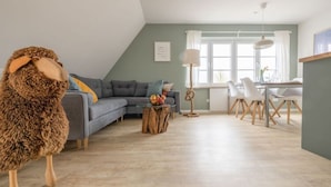 Ein modernes Wohnzimmer mit einem grauen Sofa, einem Esstisch mit Stühlen und einer großen Stofftierfigur.