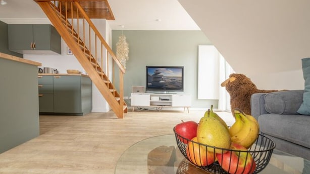 Ein modernes Wohnzimmer mit einem Glastisch, der mit Obst belegt ist, einer Couch und einem Fernseher im Hintergrund.