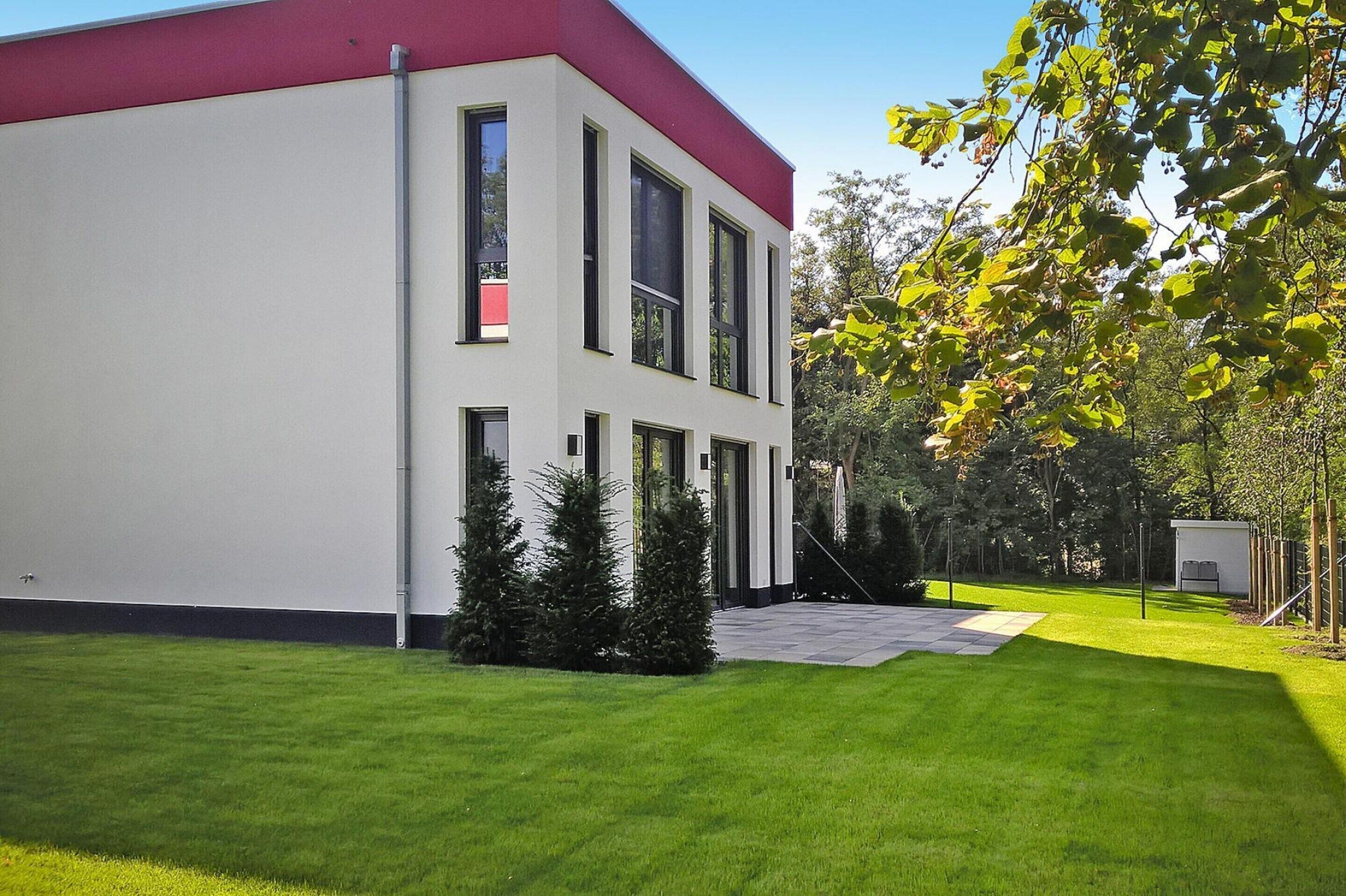 Un bâtiment moderne avec un toit rouge et des murs blancs, entouré de pelouses et d’arbres bien entretenus.
