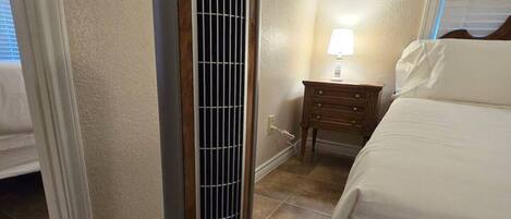 Una habitación de hotel con un radiador portátil, una mesita de noche con lámpara y una cama.