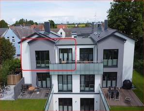 A modern two-story house with a balcony, large windows, and a deck area. - Ferienwohnung Inselresort James Cook auf Fehmarn (Fehmarn)