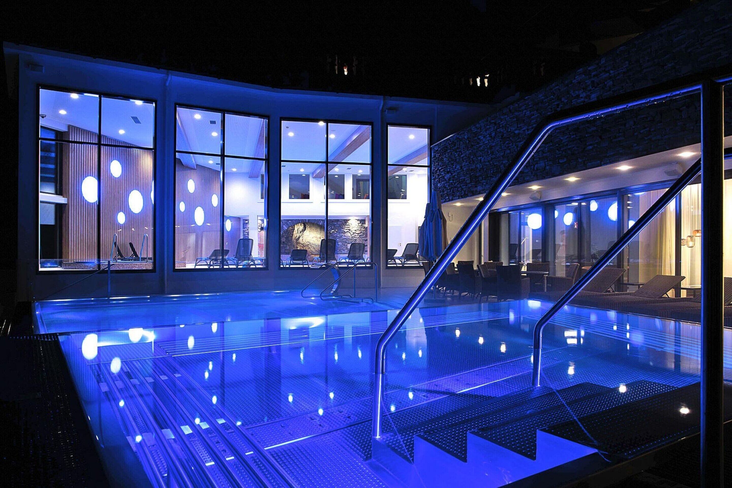Una piscina interior con barrera de vidrio, una escalera y vistas del interior del hotel.