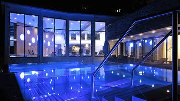 Una piscina interior con barrera de vidrio, una escalera y vistas del interior del hotel.