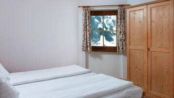 Una cama individual con cabecera de madera, una ventana con cortinas florales y un armario de madera.