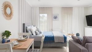 Une pièce moderne et bien éclairée, comprenant un lit, un canapé, une table à manger avec des chaises et un téléviseur fixé au mur.