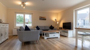 Un salon moderne avec un canapé gris, une table basse, un téléviseur et un coin repas équipé d’une banquette.