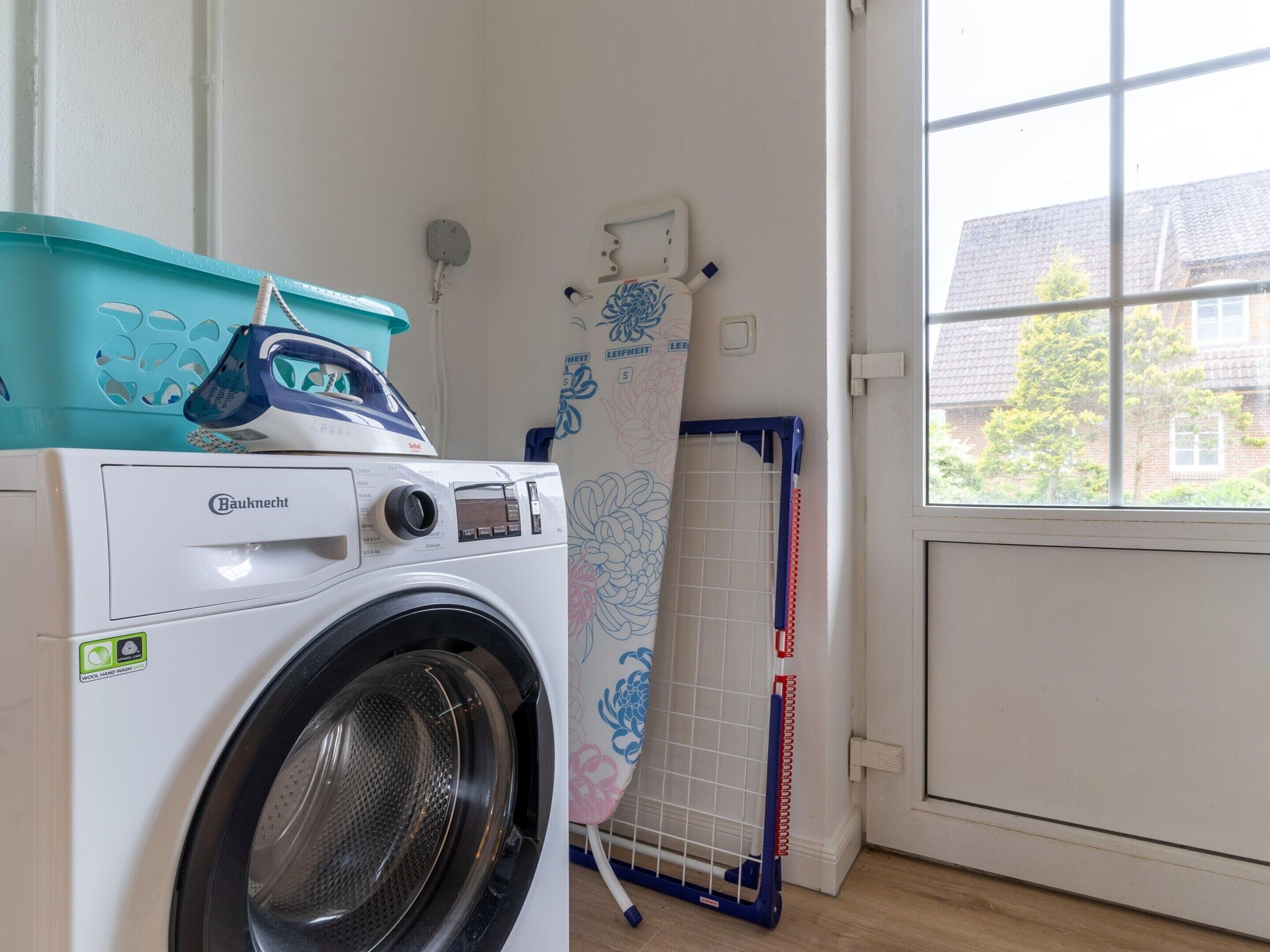 A front-loading Bauknecht washing machine in a laundry room with a window view.