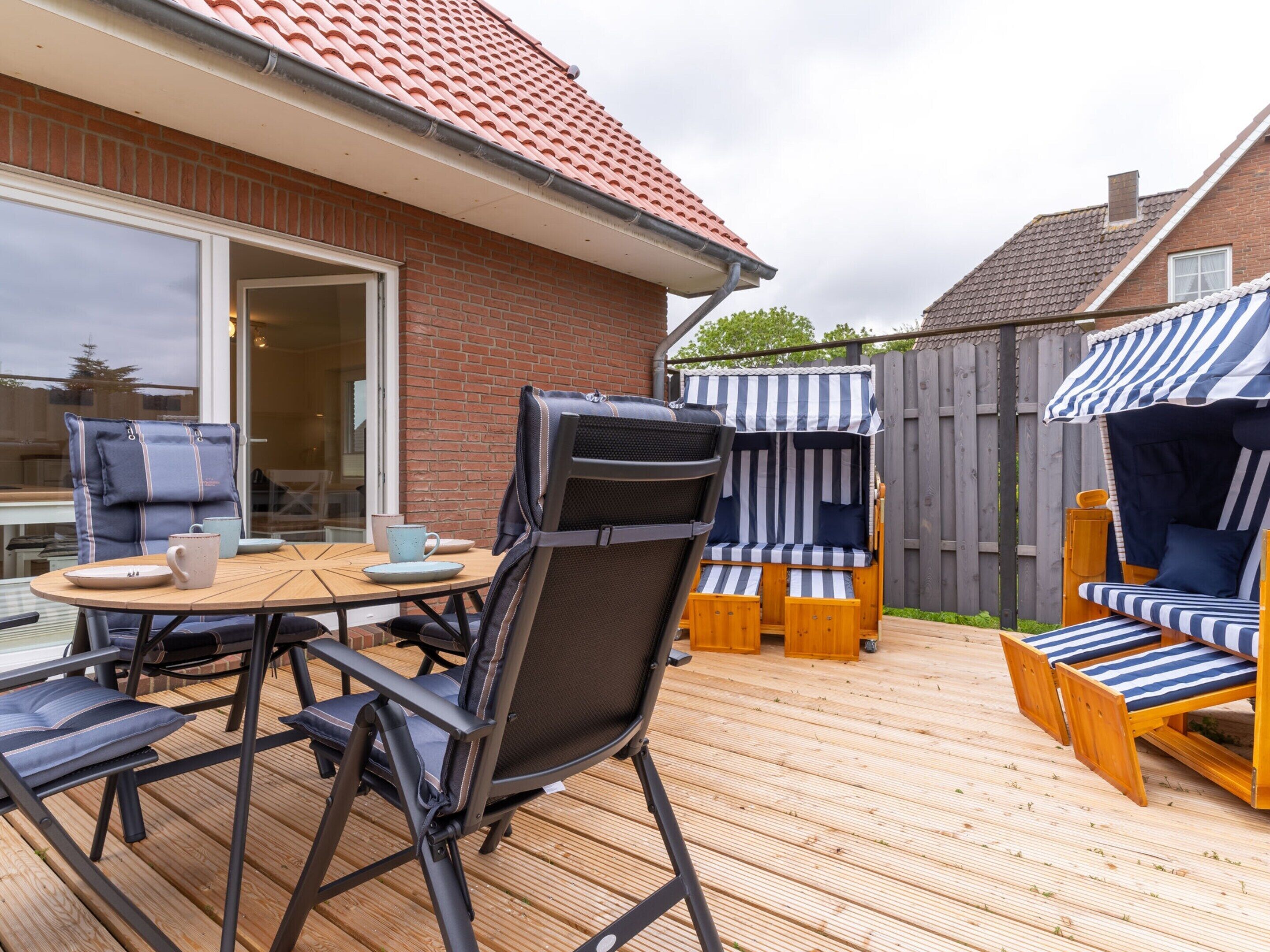 Eine Terrasse mit Tisch und Stühlen, ein überdachter Sitzbereich und ein Haus mit Backsteinfassade und Ziegeldach.