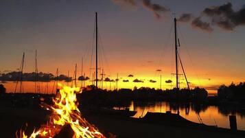 A campfire at dusk with boats and a dock in the background.